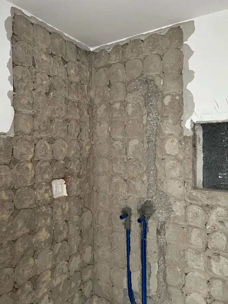 Unverputzte Bruchsteinwand mit offenen Leitungen vor der Sanierung